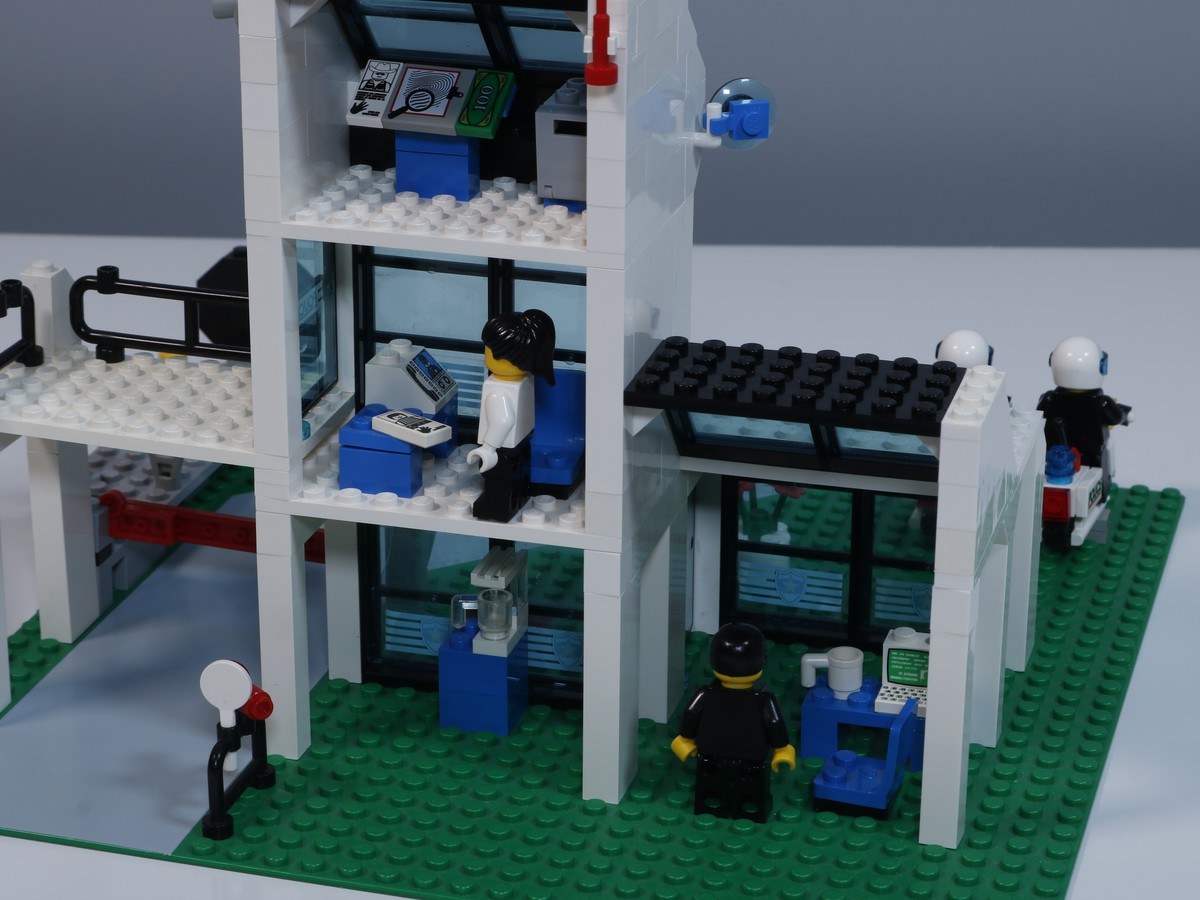 A close-up image of the back rooms of the LEGO Police Station (set 6598), highlighting various accessories and detailed features. The scene includes a various office spaces with a desks, computer screens, and police equipment. 