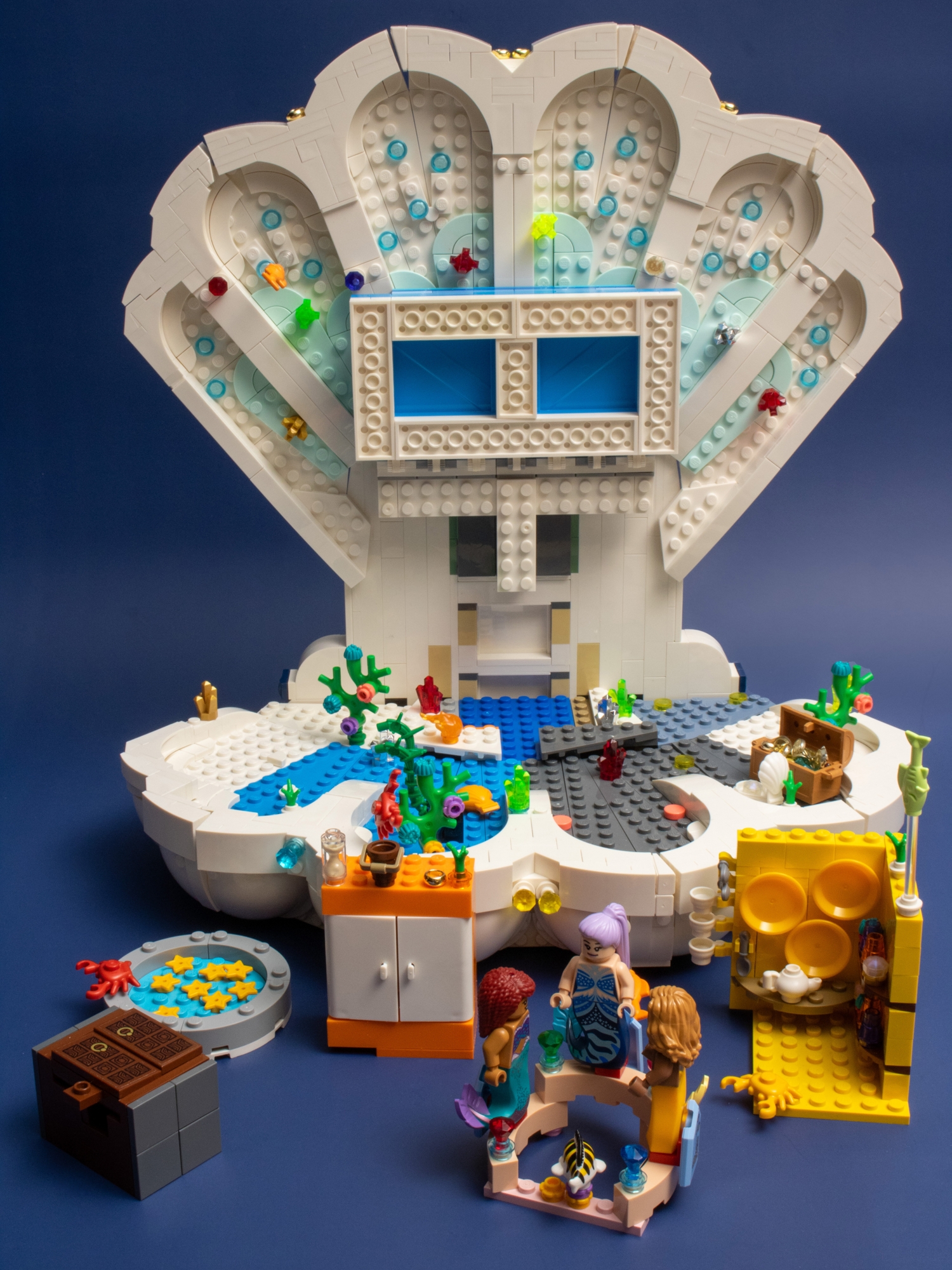 A modified LEGO Little Mermaid Royal Clamshell reimagined as a Polly Pocket-style clamshell home for mermaids. Various removable elements including a couch and wardrobe sit in front of the clamshell.