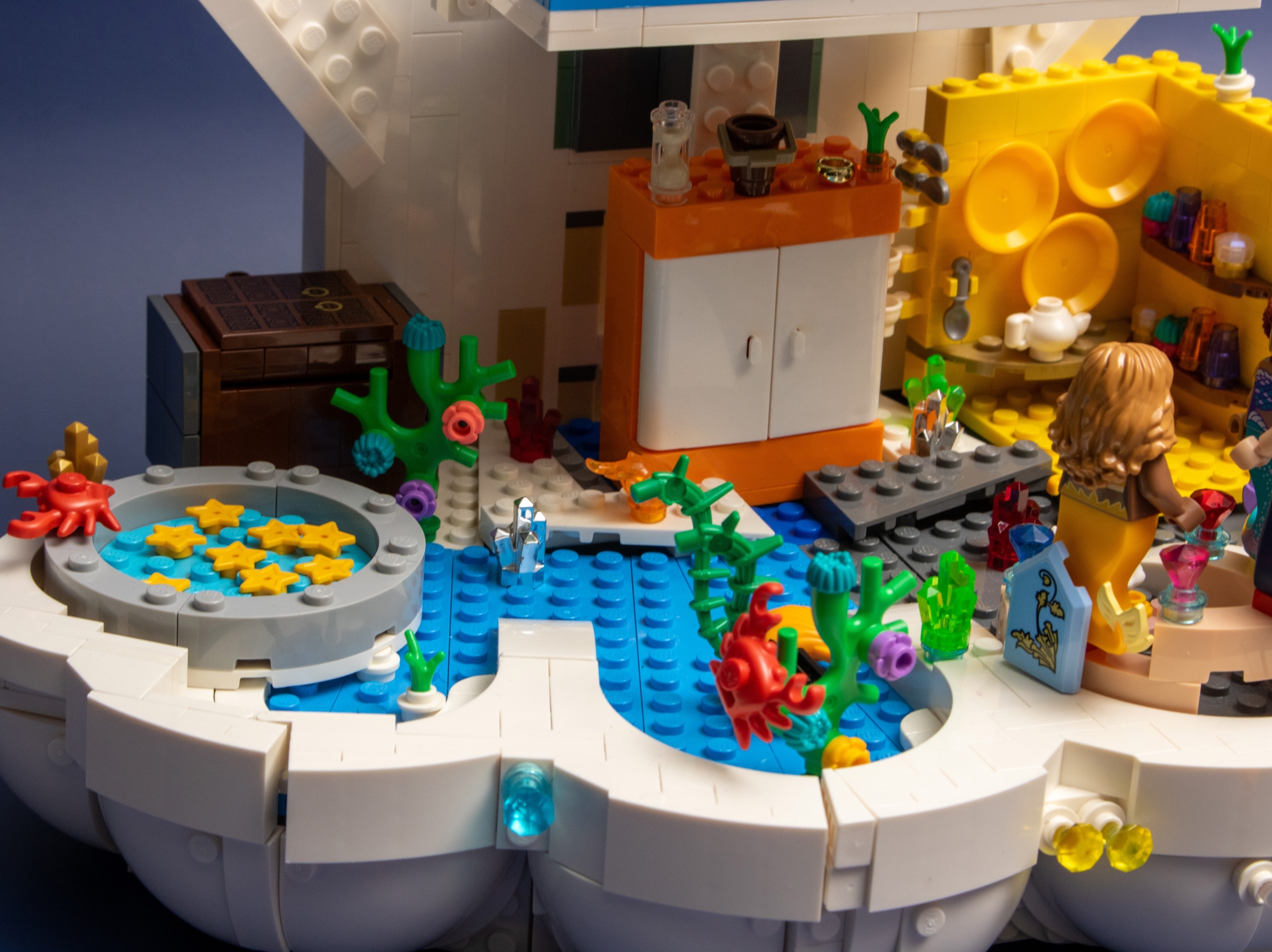 A close-up view of a modified LEGO Royal Clamshell set transformed into a Polly Pocket-style house showing a pond, storage chest, wardrobe and underwater plants. 