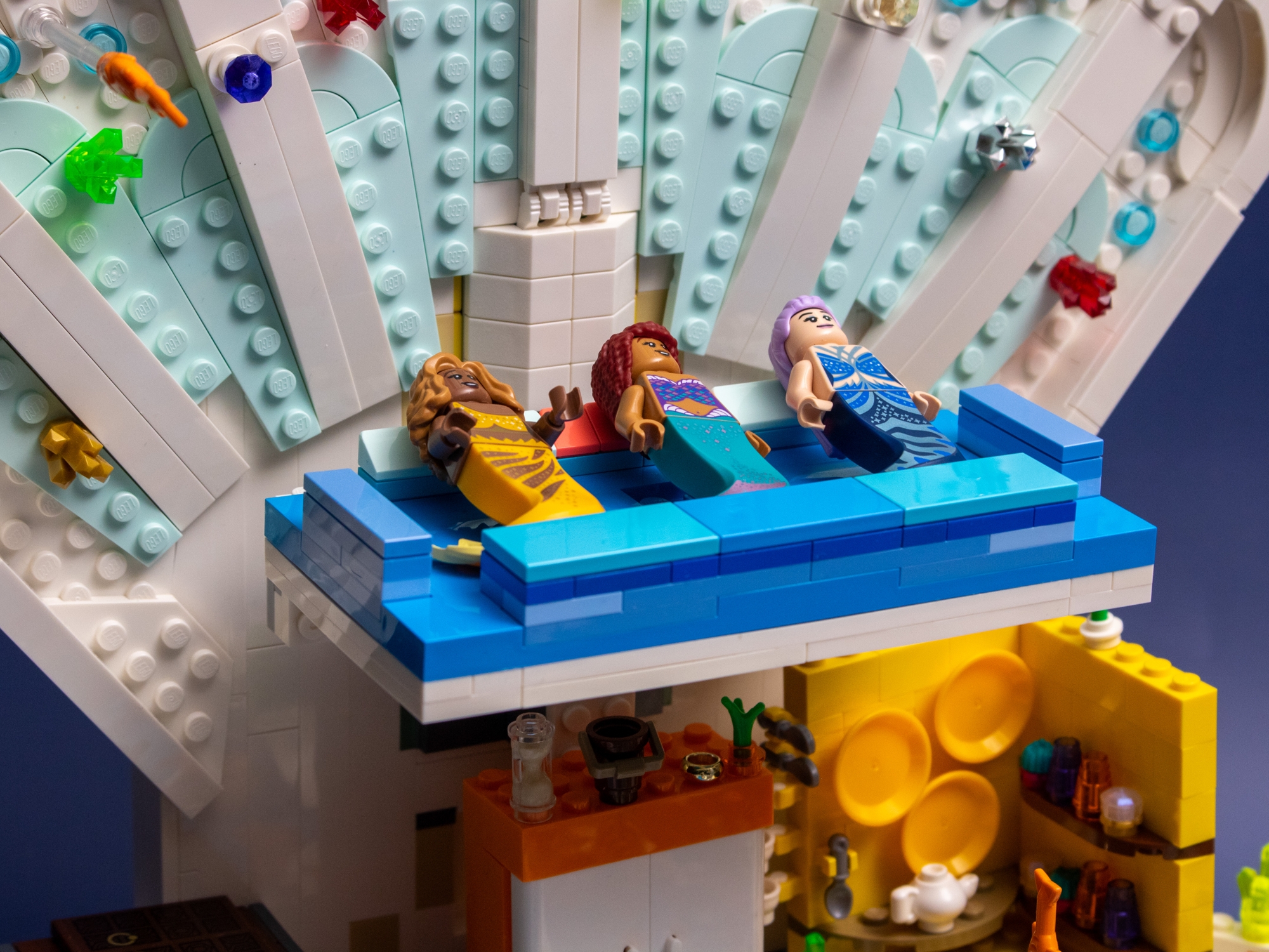 A view of the back of a modified LEGO Royal Clamshell set, reimagined as a Polly Pocket house, featuring a pull-down mermaid bed. Three mermaid minifigures are positioned on the bed. 