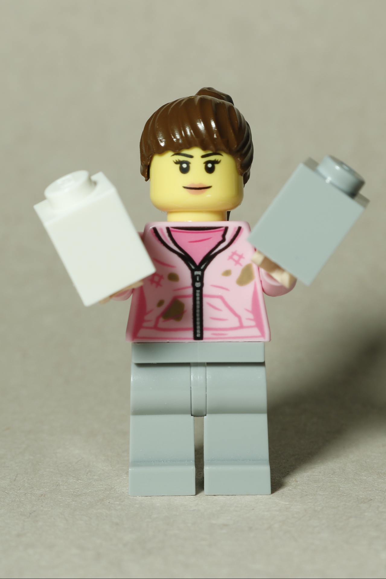 A LEGO sigfig holding a white 1×1 brick in one hand and a gray 1×1 brick in the other.